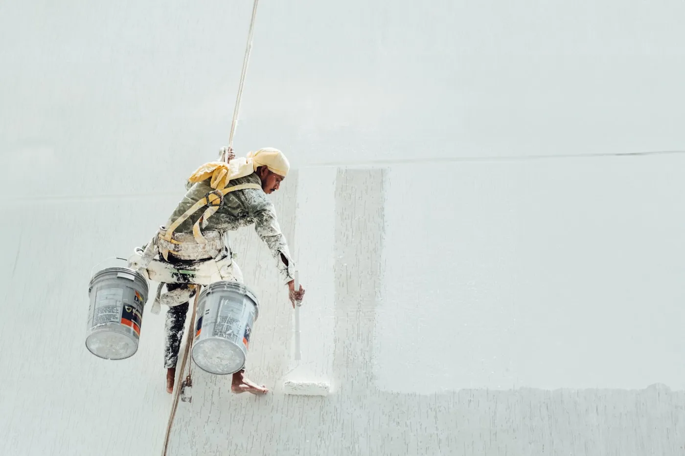 Painter working across a wall with a roller on a suspended platform