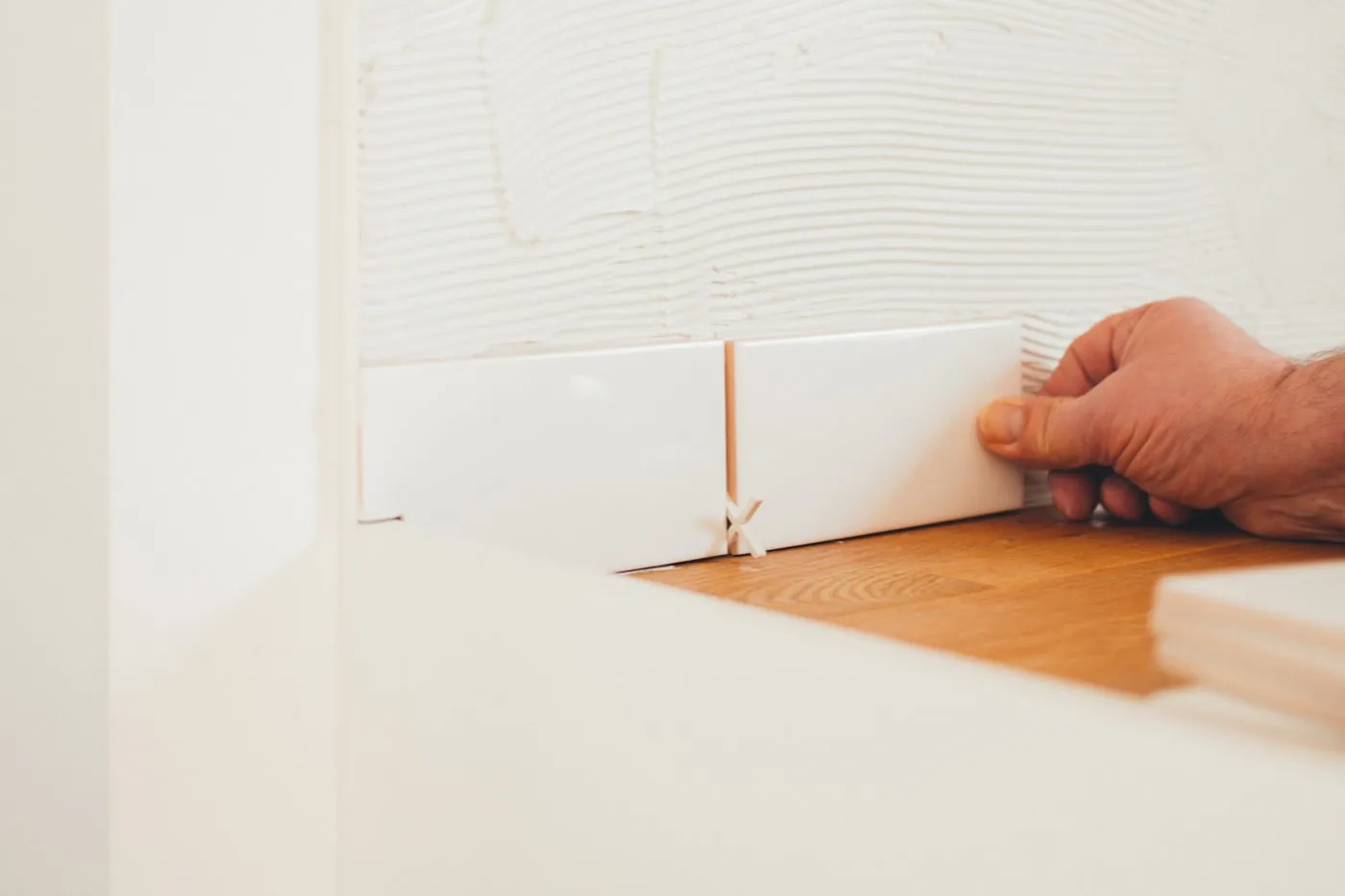 Tiler setting a white wall tile into place with spacers